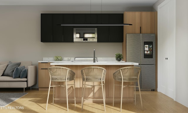 kitchen with light countertops, a sink, dark cabinets, stainless steel fridge, and a kitchen breakfast bar