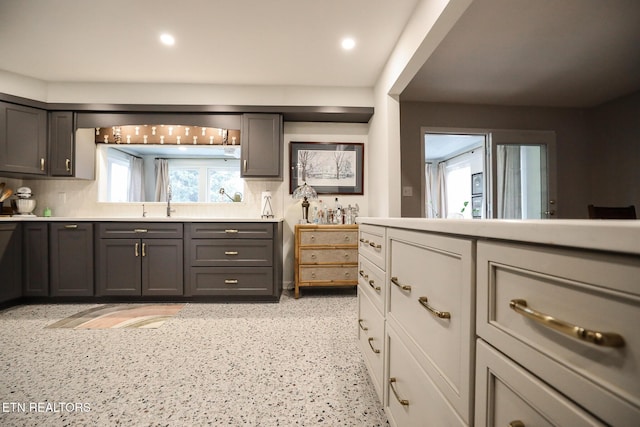 kitchen featuring recessed lighting, light countertops, backsplash, gray cabinetry, and a sink