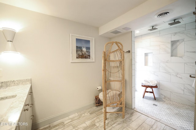 full bath with visible vents, tiled shower, vanity, and baseboards