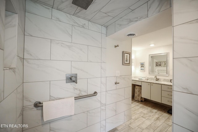 full bath featuring visible vents, a tile shower, vanity, and tile walls