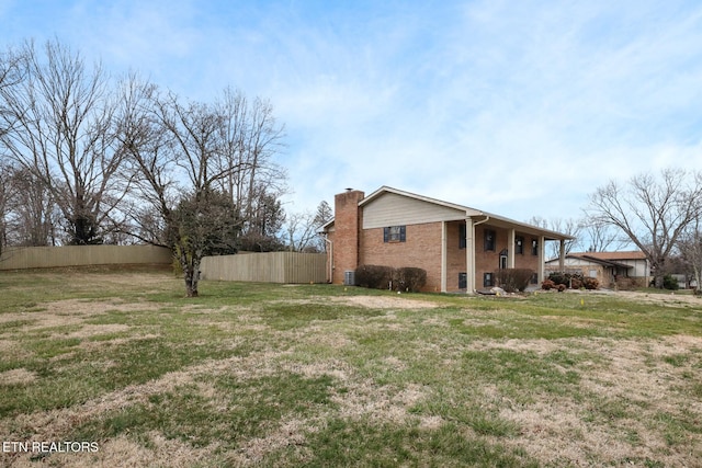 view of side of home featuring a yard, brick siding, a chimney, and fence