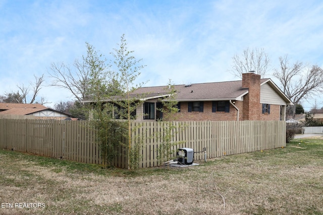 back of property featuring a chimney, fence, a lawn, and brick siding