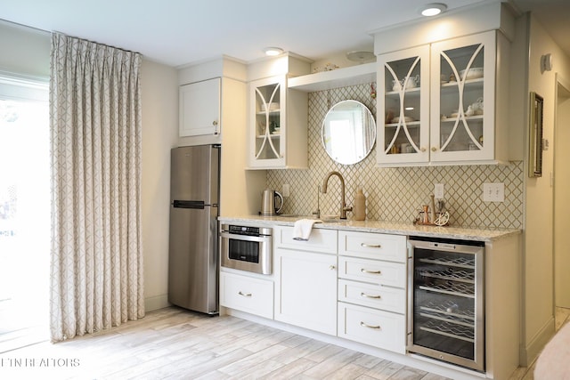 kitchen with beverage cooler, appliances with stainless steel finishes, light stone countertops, tasteful backsplash, and glass insert cabinets