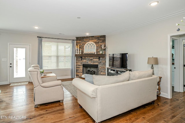 living area featuring ornamental molding, a stone fireplace, baseboards, and hardwood / wood-style flooring