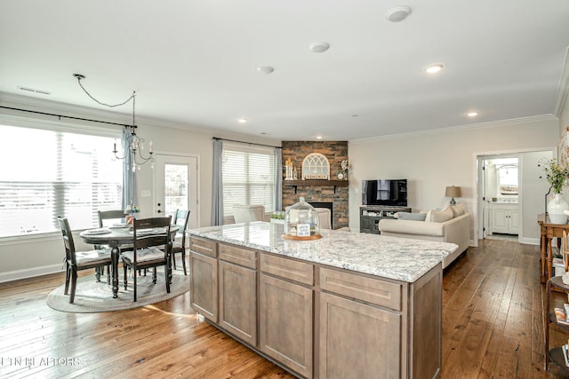 kitchen featuring crown molding, a kitchen island, a stone fireplace, light stone countertops, and hardwood / wood-style flooring