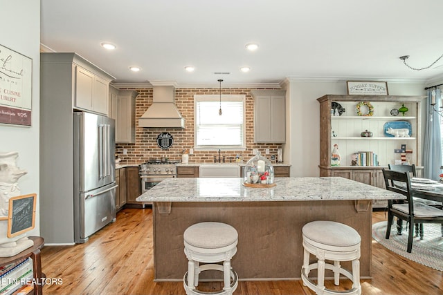 kitchen featuring high end appliances, light wood-style floors, a sink, premium range hood, and a kitchen breakfast bar