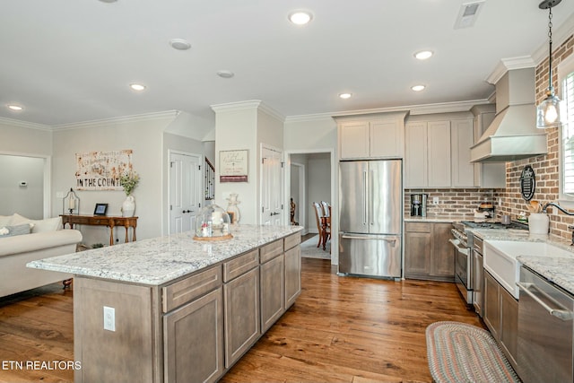 kitchen featuring decorative backsplash, high end appliances, hardwood / wood-style floors, a center island, and light stone countertops