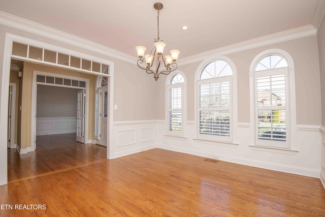 unfurnished dining area featuring an inviting chandelier, crown molding, wood finished floors, and a wainscoted wall