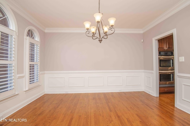 spare room with a chandelier, a wainscoted wall, light wood-style flooring, and crown molding