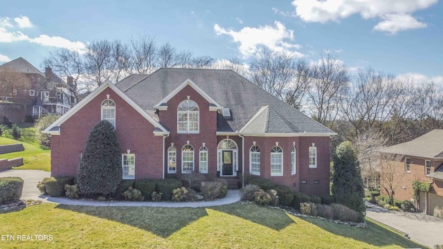 traditional-style home featuring brick siding, a front yard, and a shingled roof