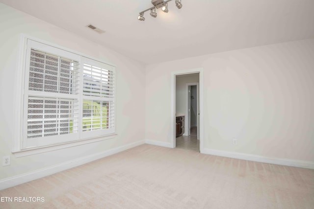 unfurnished room with light carpet, baseboards, visible vents, and track lighting