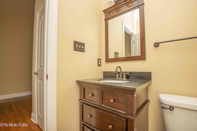 half bathroom featuring toilet, wood finished floors, vanity, and baseboards