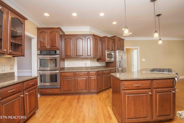 kitchen featuring light wood-style flooring, ornamental molding, appliances with stainless steel finishes, light stone countertops, and decorative light fixtures