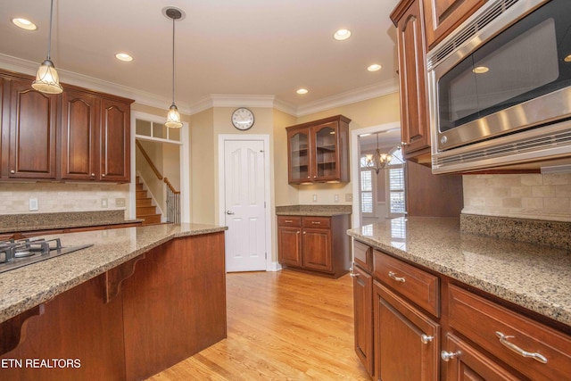 kitchen featuring stainless steel appliances, light wood finished floors, hanging light fixtures, and light stone counters