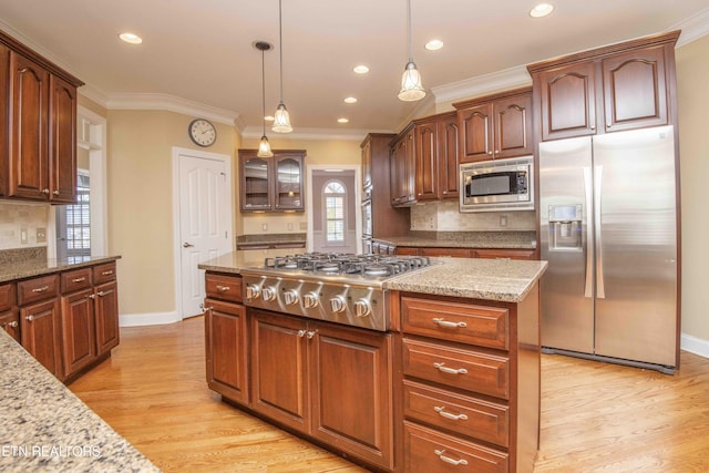 kitchen with light wood finished floors, appliances with stainless steel finishes, hanging light fixtures, light stone countertops, and crown molding