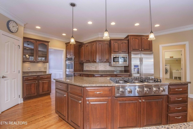 kitchen featuring washer / dryer, a center island, stainless steel appliances, crown molding, and light wood-style floors