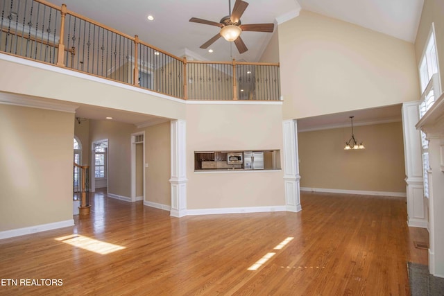 unfurnished living room featuring a fireplace, baseboards, wood finished floors, ornate columns, and ceiling fan with notable chandelier