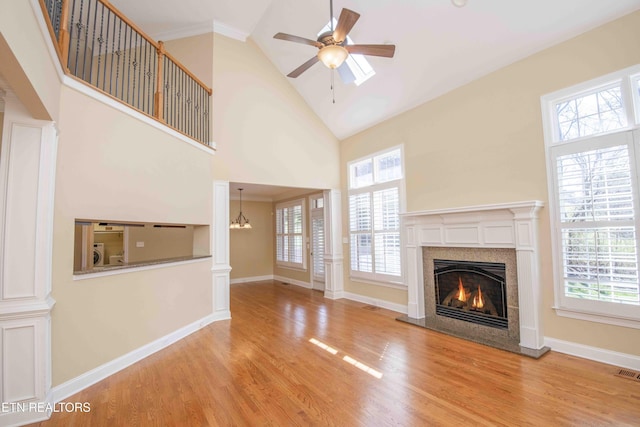 unfurnished living room with a warm lit fireplace, high vaulted ceiling, plenty of natural light, and wood finished floors