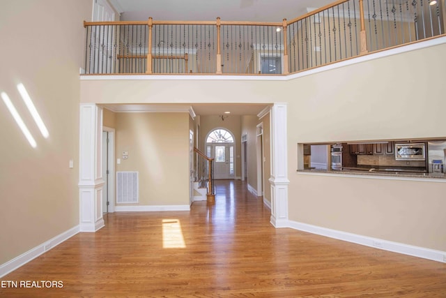 foyer entrance featuring wood finished floors, a towering ceiling, visible vents, baseboards, and stairway