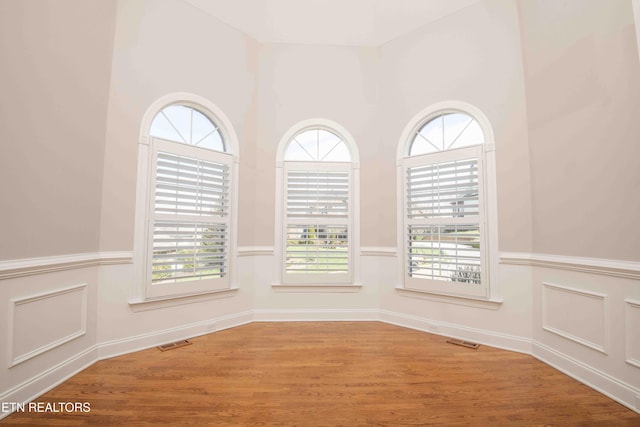 empty room featuring visible vents, a decorative wall, wood finished floors, and wainscoting