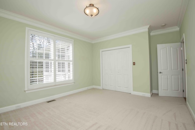 unfurnished bedroom with baseboards, visible vents, light colored carpet, ornamental molding, and a closet