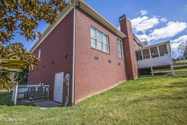 view of property exterior with a sunroom, a chimney, a lawn, and brick siding