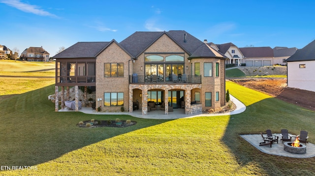 rear view of property featuring a patio, a balcony, a fire pit, brick siding, and a lawn