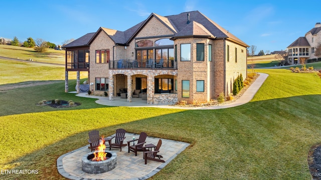 back of property with a balcony, a fire pit, brick siding, a lawn, and a patio area