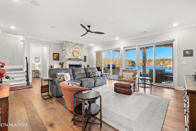 living area featuring stairs, crown molding, a stone fireplace, and wood finished floors