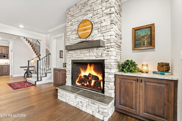 living room with stairway, ornamental molding, a stone fireplace, wood finished floors, and baseboards