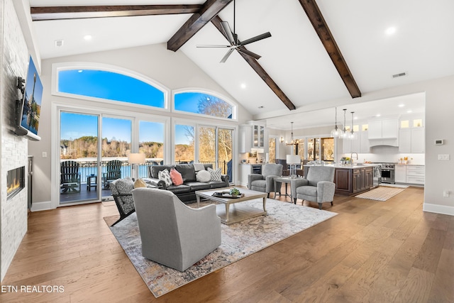 living area featuring high vaulted ceiling, light wood-type flooring, visible vents, and a stone fireplace