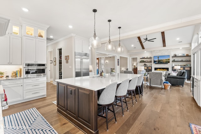 kitchen with white cabinets, wood-type flooring, stainless steel appliances, light countertops, and a fireplace