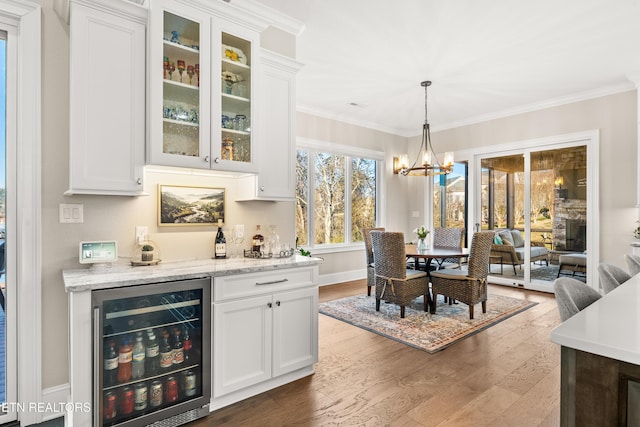 interior space featuring a dry bar, beverage cooler, ornamental molding, wood finished floors, and a notable chandelier