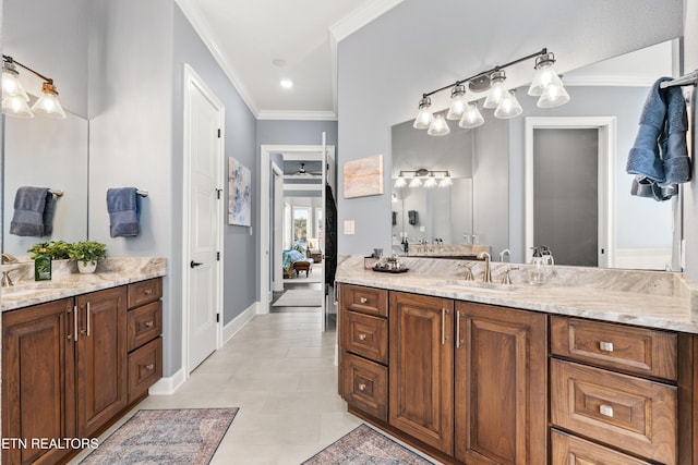 ensuite bathroom featuring baseboards, two vanities, crown molding, and a sink