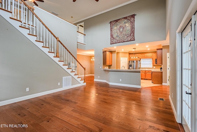 unfurnished living room with baseboards, visible vents, light wood-style flooring, ceiling fan, and stairs