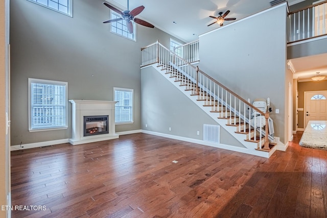 unfurnished living room with stairs, hardwood / wood-style flooring, visible vents, and baseboards