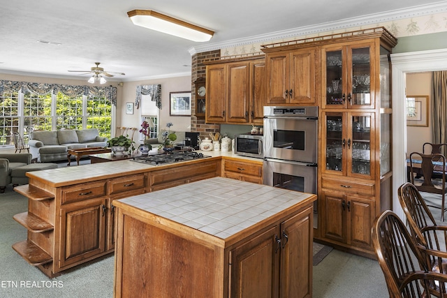 kitchen featuring brown cabinets, a peninsula, stainless steel appliances, and tile counters