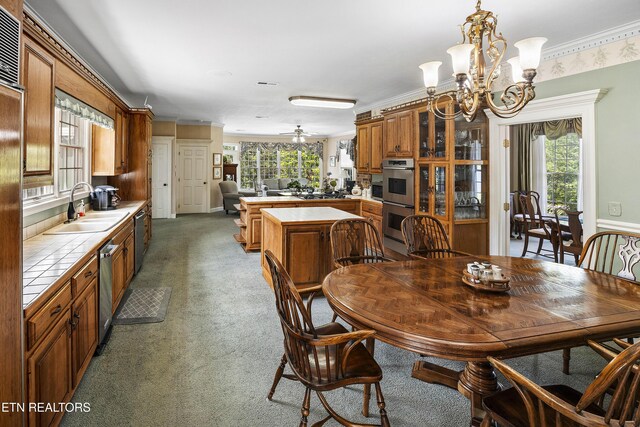 carpeted dining room with ornamental molding, ceiling fan with notable chandelier, and a sink