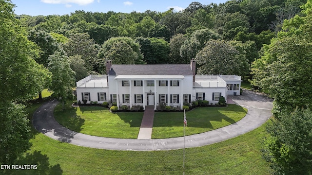 exterior space featuring a forest view, a chimney, and a front lawn