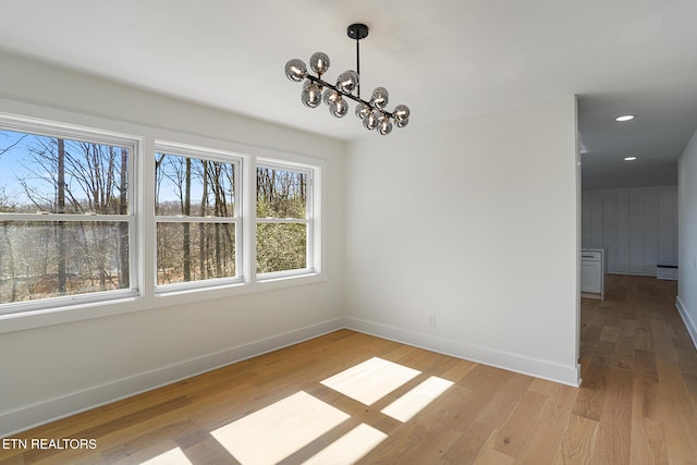 unfurnished dining area featuring light wood-style floors, recessed lighting, a notable chandelier, and baseboards