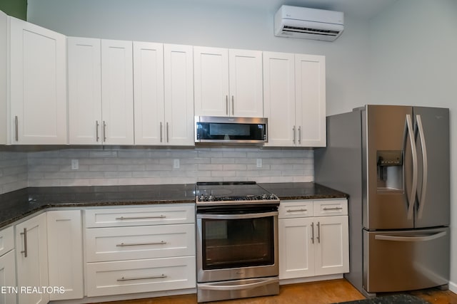 kitchen with a wall mounted air conditioner, backsplash, white cabinetry, stainless steel appliances, and dark stone counters