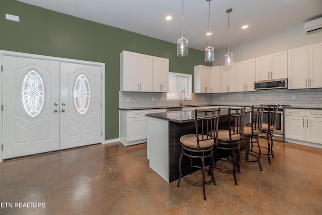 kitchen with a sink, dark countertops, white cabinetry, stainless steel appliances, and a breakfast bar area