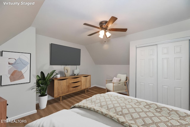 bedroom with a ceiling fan, wood finished floors, baseboards, lofted ceiling, and a closet