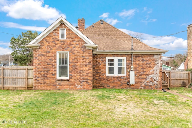 rear view of house with brick siding, a shingled roof, fence, a lawn, and a chimney