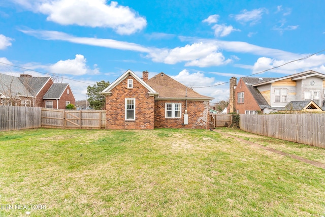 back of property with brick siding, a yard, a chimney, and a fenced backyard