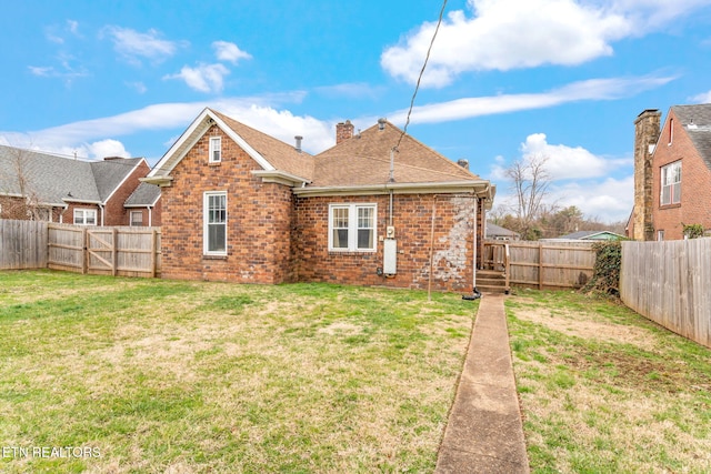 rear view of house featuring brick siding, roof with shingles, a chimney, a lawn, and a fenced backyard