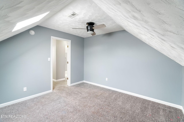 additional living space featuring visible vents, carpet flooring, a textured ceiling, vaulted ceiling with skylight, and baseboards