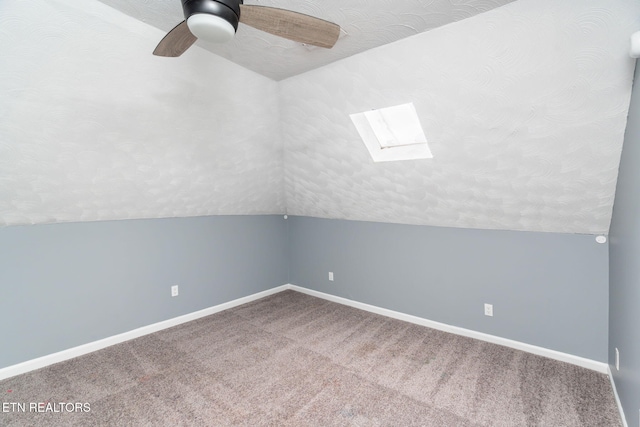 carpeted spare room with lofted ceiling with skylight, baseboards, and a textured ceiling