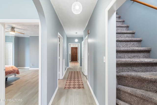 hall featuring arched walkways, light wood-style flooring, baseboards, ornamental molding, and stairway