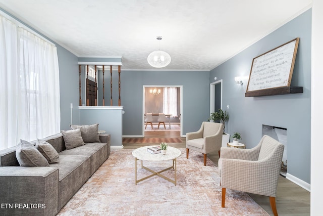 living room featuring a fireplace, an inviting chandelier, ornamental molding, wood finished floors, and baseboards